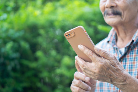 Cropped image of smiling senior man text messaging through mobile phone on nature background. Selective focus.の写真素材