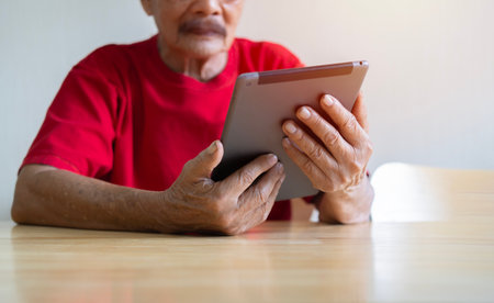 Handsome old man in red T-Shirt is using a digital tablet, looking at camera while working at home. Selective focus.の写真素材