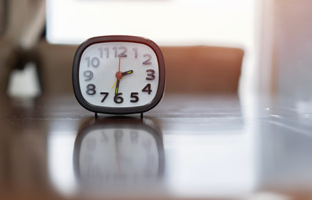 Black and white alarm clock on wooden table with blurred background, selective focus