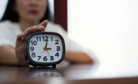Female hand turning off black and white alarm clock at workplace. Selective focus and close up at alarm clock, business education conceptの写真素材