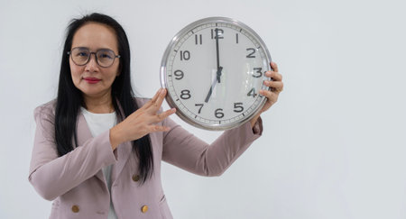 Smiling Asian business woman in eyeglasses holding clock and looking at the camera over white backgroundの写真素材