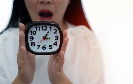 Photo of pretty Asian woman hold alarm clock and open mouth funny wearing white shirt with sunlight...