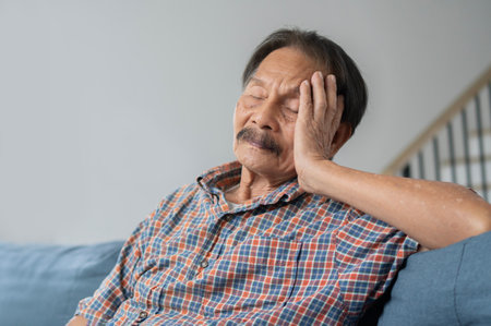 Tired elderly Asian man relax fall asleep on comfortable couch in living room, exhausted mature male take nap daydreaming on cozy sofa at home.の写真素材