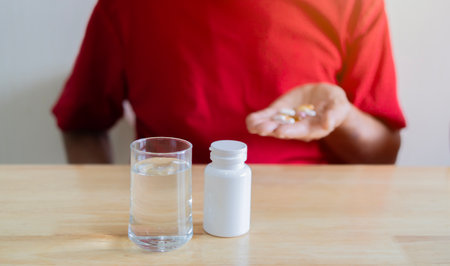 Cropped image of senior man in red T-Shirt taking medicine pill at home. Age, medicine, health care and people concept. Selective focus at subject.の写真素材