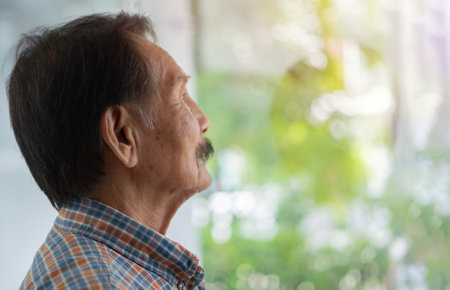 Side view portrait of Asian elderly man wearing striped shirt standing and look outside, copy spaceの写真素材