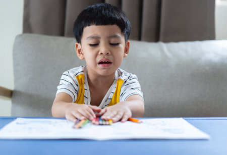 Little adorable Asian child boy holding colored pencils depressed and worry for distress, crying angry and afraid. sad expression.の写真素材