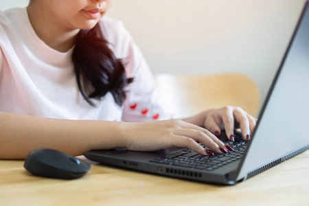 Shot of confident young Asian woman worker sit at office table by laptop search data browse corporate network for business news. Selecitve focus on hand.の写真素材