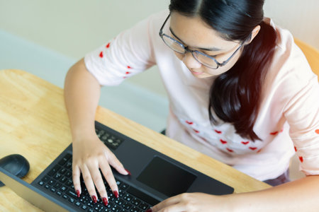 Top view of young Asian female with glasses writer keyboarding on laptop while working for online...