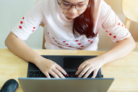 Top view of teen girl with laptop in her room while sitting at the desk and writing on her laptop....