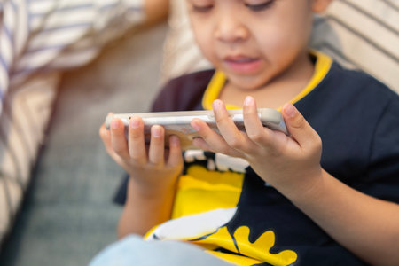 Little small boy 3-4 years old in dark blue t-shirt play racing app on gadget smartphone for pc video games. Selective focus on hand.の写真素材
