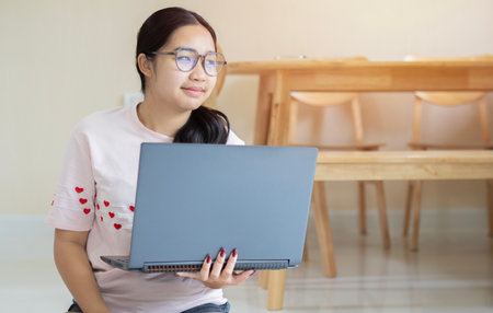 Beautiful cheerful blackhead girl wear glasses using dark silver laptop while sitting on floor in...