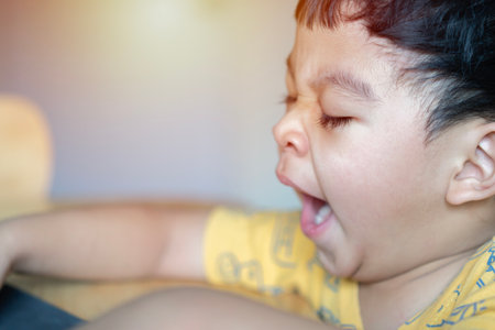 Time to go to bed. Cute Asian little boy opening mouth widely, yawning, feeling tired and sleepy, looks like dozing off. Side view, selective focus.の写真素材