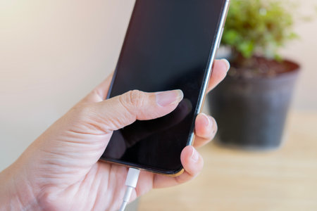 Close up of woman hands plugging a charger in a smart phone. Woman using smartphone with powerbank. Selective focus on hand.の写真素材
