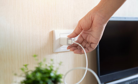 Hand ready to plug or unplug white power cord cable mobile phone charger charts Into electric socket...