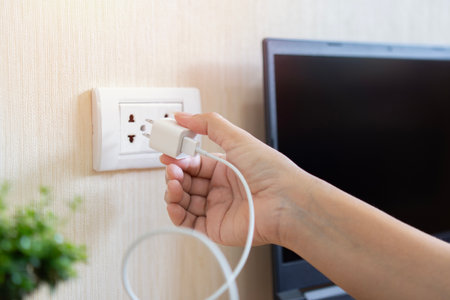 Closeup of the hands of a woman plugging in or plug of her smartphone into a socket on the desk.の写真素材