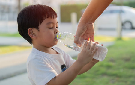 Mother giving a bottle of clean water to her son and help him to dringking fresh water from plastic...