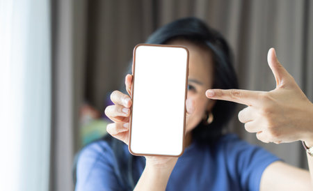 Smiling happy woman of Asian in blue sweater point finger on mobile cell phone with blank screen....