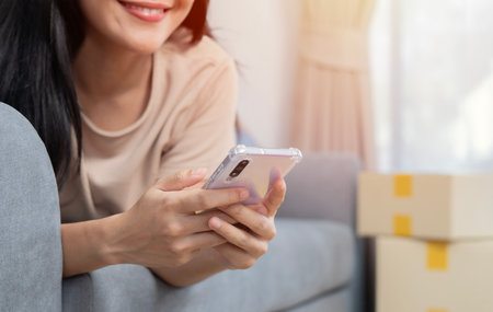 Attractive young woman is moving, lying on sofa among cardboard boxes, using a smartphone and smiling. Service on mobile phone concept.の写真素材