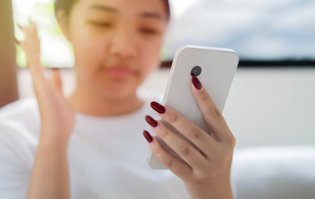 Asian teenager say hi with friend online virtual by social distance videocall using smartphone while sitting in livingroom. Selective focus on hand.の写真素材