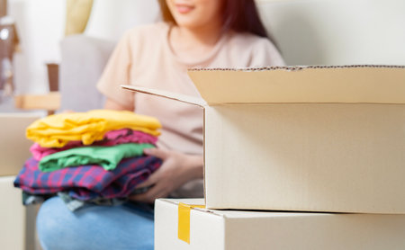 Happy asian young woman, packing stuff clothes, give second hand for donate, check list object in...