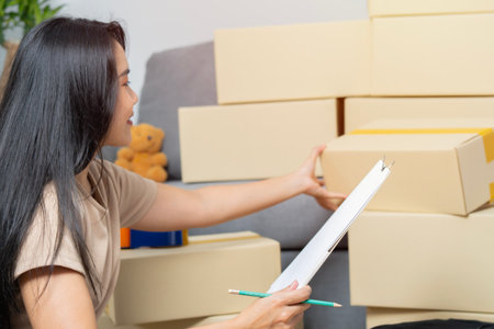 Young hispanic Asian woman smiling confident while reading and checking list of boxes at new home. Move concept.の写真素材