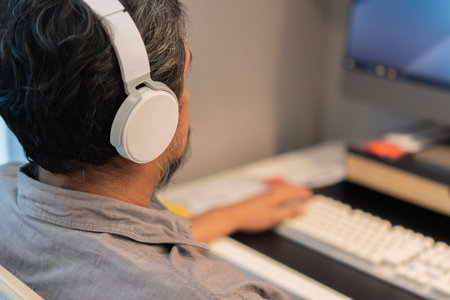 View from the shoulder of businessman in shirt working inside office using computer with headphones...
