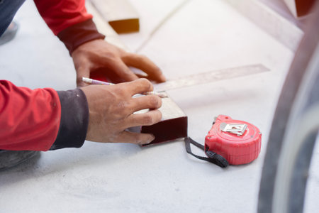 Close up of worker measuring aluminium construction frame with steel ruler and yellow tape. Selctive...