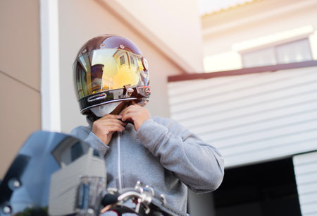 Ready to ride. Man sitting on a motorcycle, wearing a gray jacket and fastening his helmet over parking garage.の写真素材
