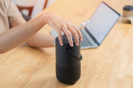 Selective focus of woman hand with laptop using voice assistant speaker at home office. Portable...