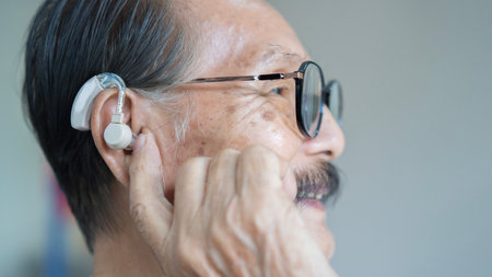 Side view close up picture of a senior Asian man inserting a hearing aid and adjust it in his ear. Selective focus, copy space.の写真素材