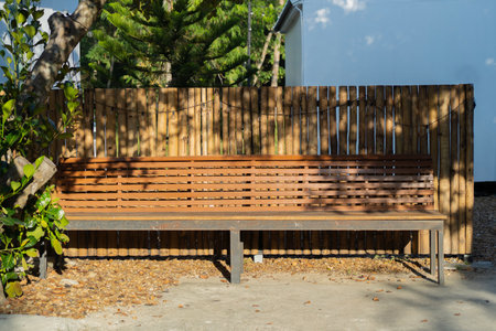 A long modern wooden bench and small bamboo fence in the park against a background of plants and...