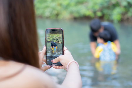 Cropped image of young Asian mom take a picture of a little son and husband playing in river on warm and sunny summer dayの写真素材