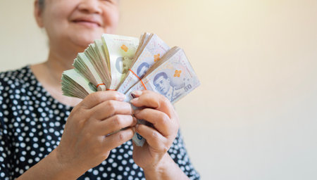 Happy older Asian woman holding a lot of Thai money that she has won, feeling excited. Retirement concept.の写真素材