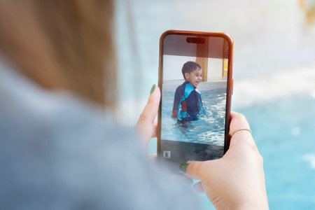 Mother making photo of her son playing or jumping in water of swimming pool on summer day.の写真素材