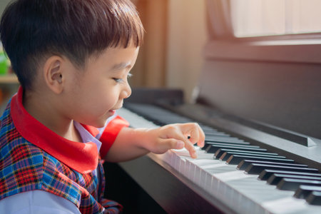 Side view portrait of little piano player smiling and playing the piano with the light shining from the window. Learning to play music concept.の写真素材