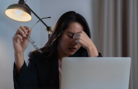 Tired young  Asian woman feel pain eyestrain holding glasses rubbing dry irritated eyes fatigued...