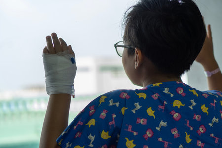 Child patients in the hospital are adding saline solution on hand , stand at the window to look out. Back view.の写真素材
