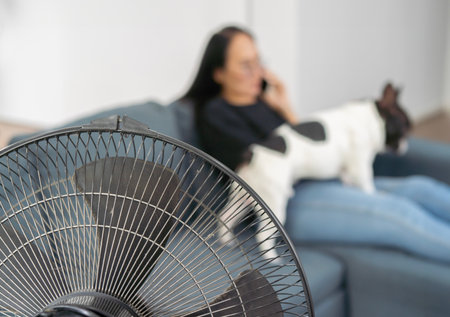 Soft blurr of cute french bulldog and ower enjoying air flow from fan on sofa indoors. Summer heat, selective focus.の写真素材