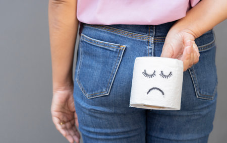 Woman holds toilet paper with sad face, standing on light gray background. Selcective focus....