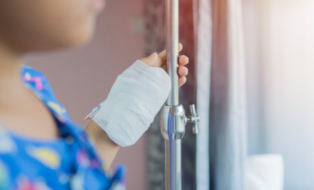 A child stands in a hospital ward with saline solution drip and looks out the window in a hospital....