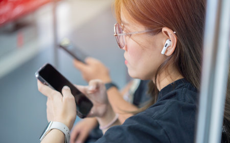 Young Asian woman sitting in a subway car and listening music with her smartphone by wireless...