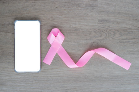 Pink awareness ribbon and smartphone with blank screen on wooden background. Copy space.の写真素材