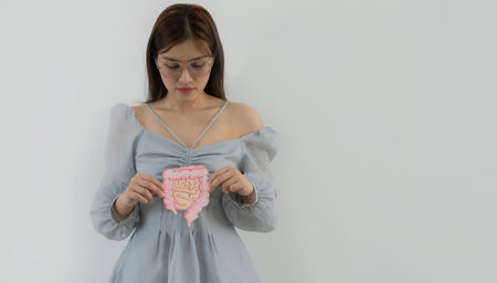 Portrait picture of young Asian woman holding intestine shape and looking happily over white wall...