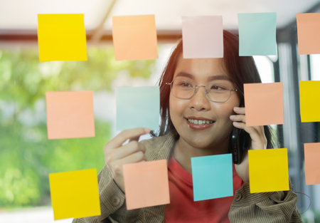 Businesswoman using smartphone and writing on post it note, Brainstorming session with post it notes at office. Selective focus.の写真素材
