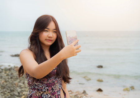 Portrait picture of happy Asian young woman with mobile phone on a beach, Thailand.