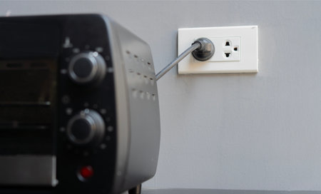 Shot image of black mini electric oven with plugin outlet power at wall background. Selective focus...