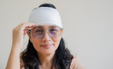 Happy emotional senior Asian woman, she has shiner under eye, wears bandage around injured head....