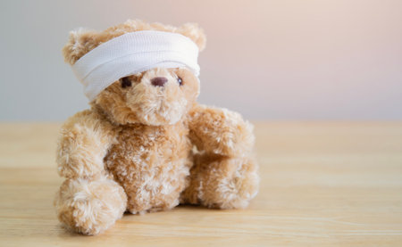 The child is hurt. Teddy bear with bandage sit on wooden table with space for text. Selective focus.の写真素材