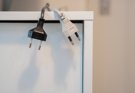 Black and white electric plugs hanging from the sideboard cabinet at office. Close up, copy space.