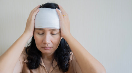 Portrait of a senior Asian woman close her eyes and touch her head with bandaged for an injury. Copy...
